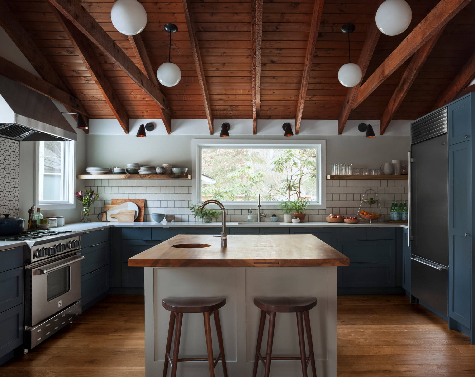 Cocina azul oscura con módulo central claro bajo techo marrón de vigas